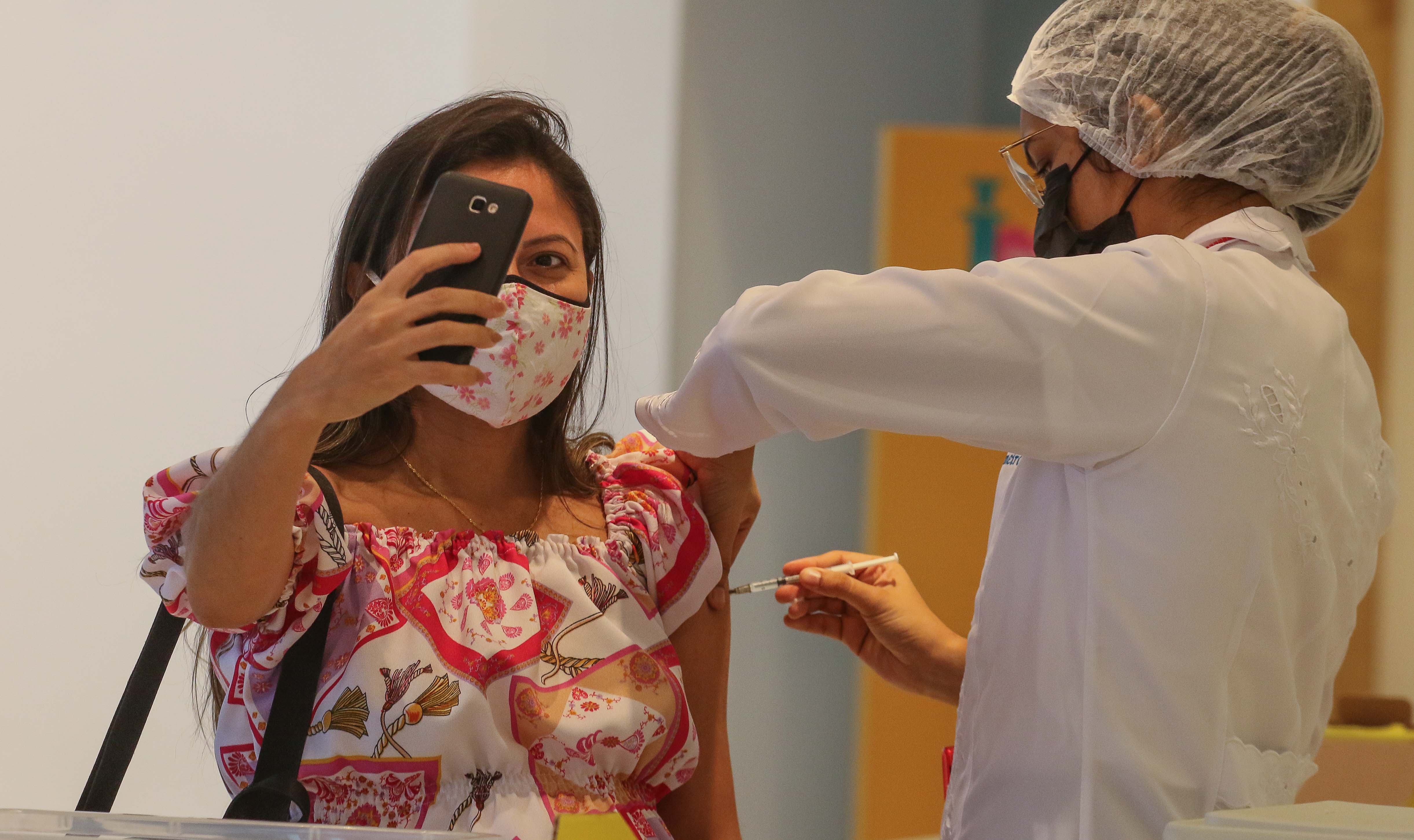 mulher faz selfie enquanto é vacinada por uma enfermeira